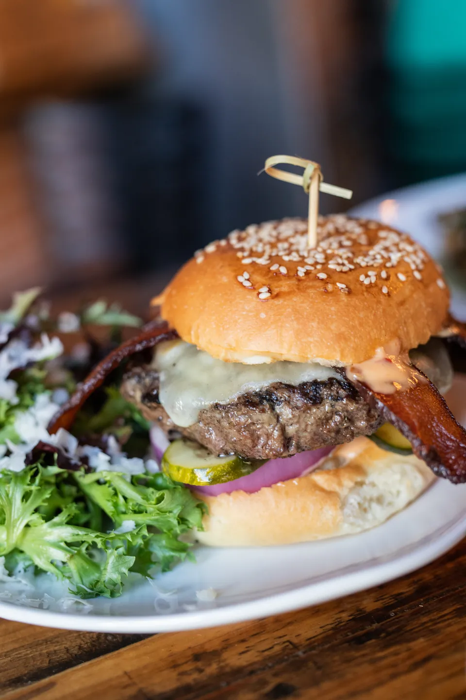 The El Moro Burger on a sesame bun with melted cheese, bacon, pickle and red onion, with a side of greens